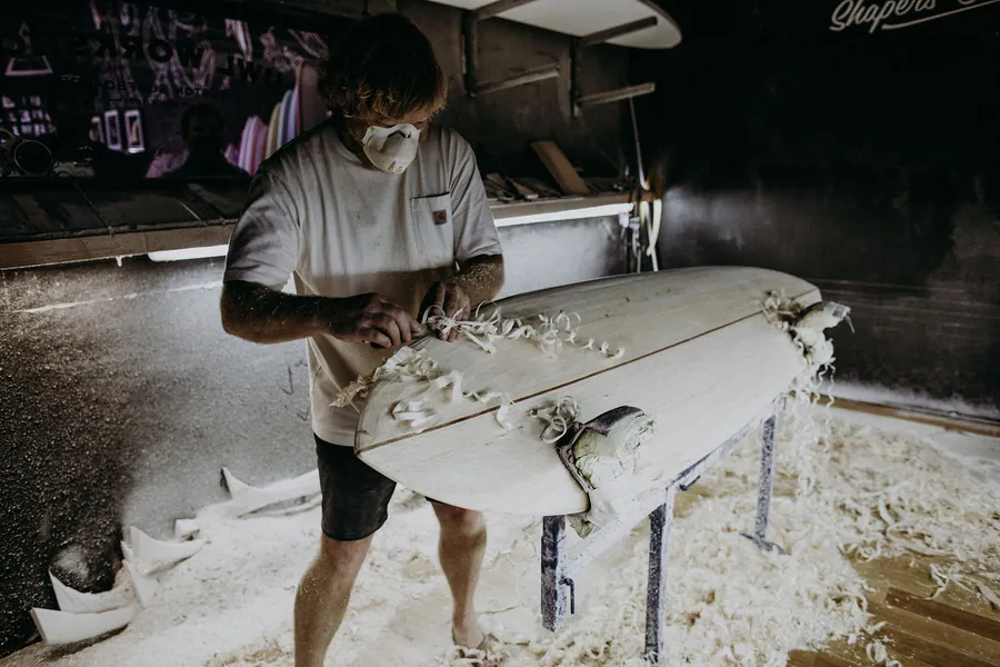 Joshua Martin shape un longboard à la main dans son atelier